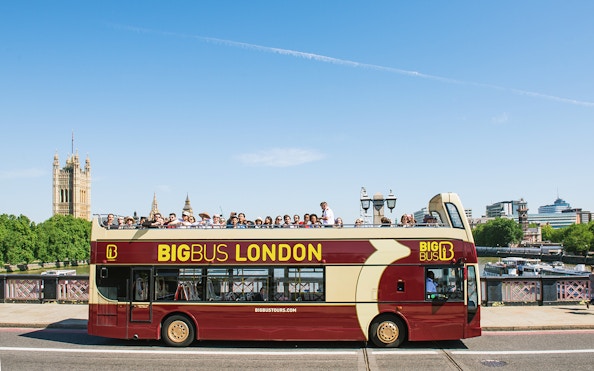 Open-top bus tour in London with tourists, passing by the Houses of Parliament.