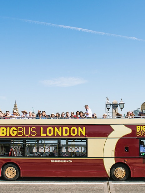 Open-top bus tour in London with tourists, passing by the Houses of Parliament.