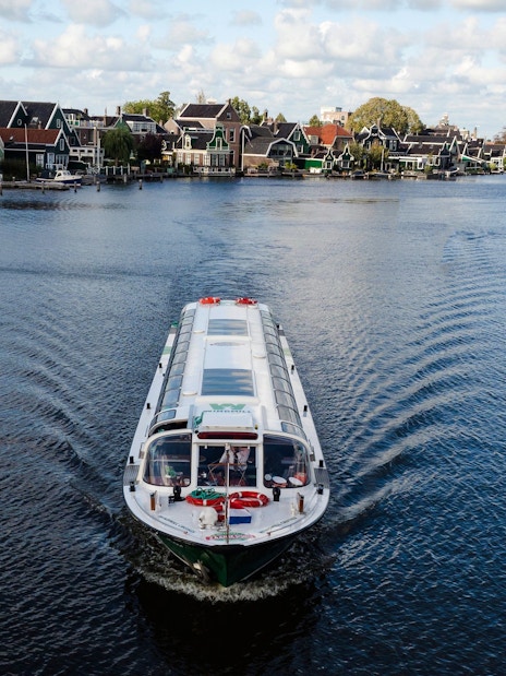 Cruise boat on a canal in Amsterdam with windmills and traditional houses in the background.