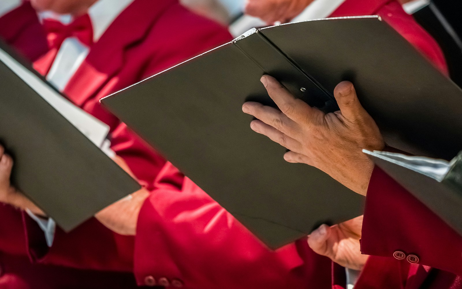 Mens choir members in red jackets holding singing books.