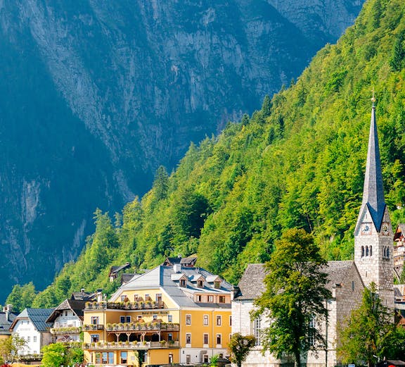 Colorful buildings and church by Hallstatt Lake, Austria, with mountains in the background.