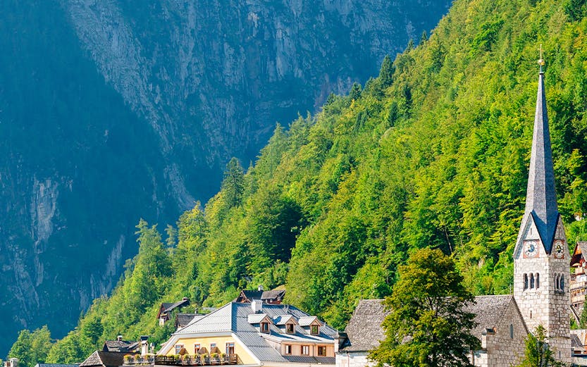 Colorful buildings and church by Hallstatt Lake, Austria, with mountains in the background.