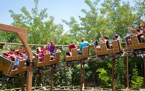 Roller coaster ride with passengers at Isla Magica, Seville, surrounded by greenery.