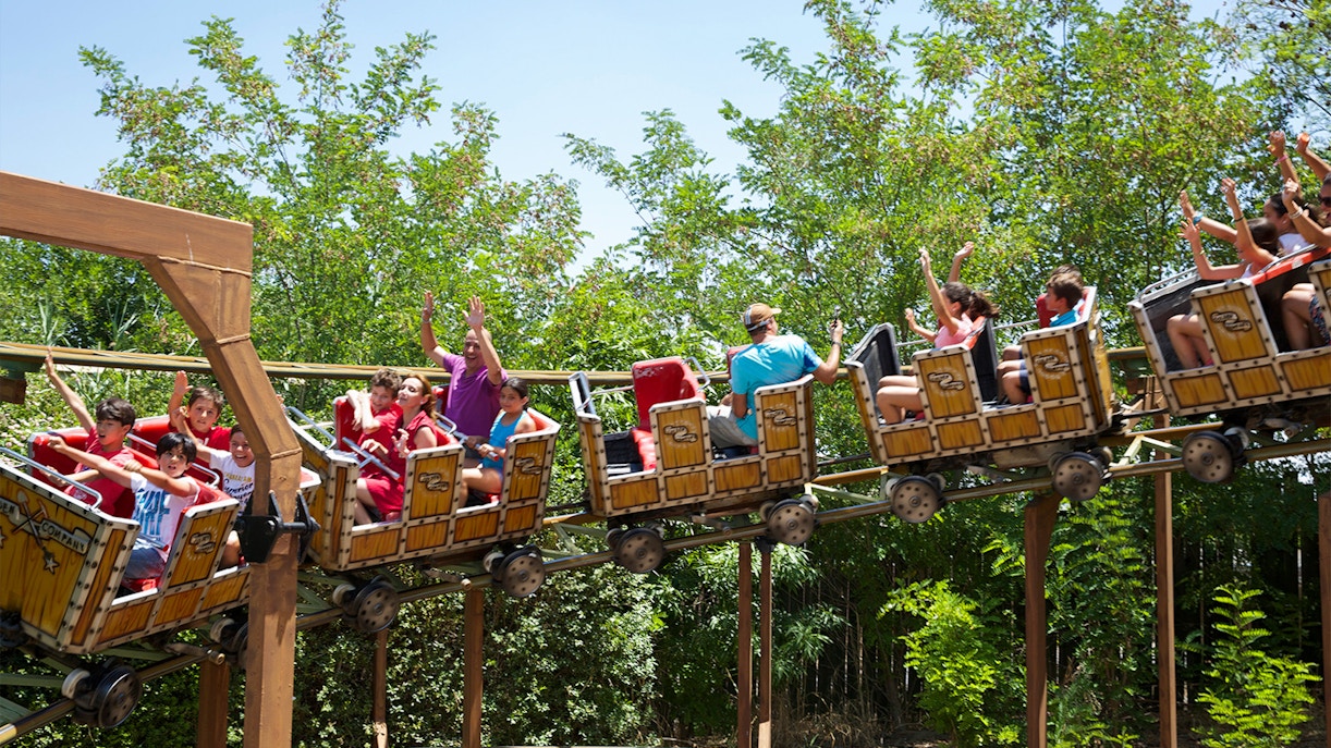 Roller coaster ride with passengers at Isla Magica, Seville, surrounded by greenery.