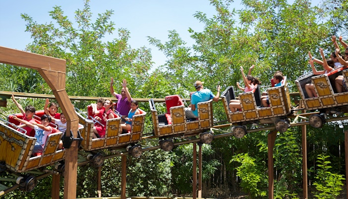Roller coaster ride with passengers at Isla Magica, Seville, surrounded by greenery.