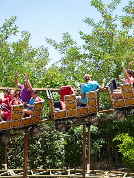 Roller coaster ride with passengers at Isla Magica, Seville, surrounded by greenery.