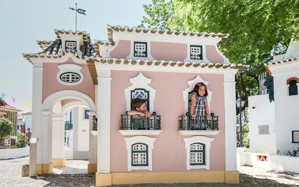 Children peering from windows of a miniature house at Portugal dos Pequenitos.