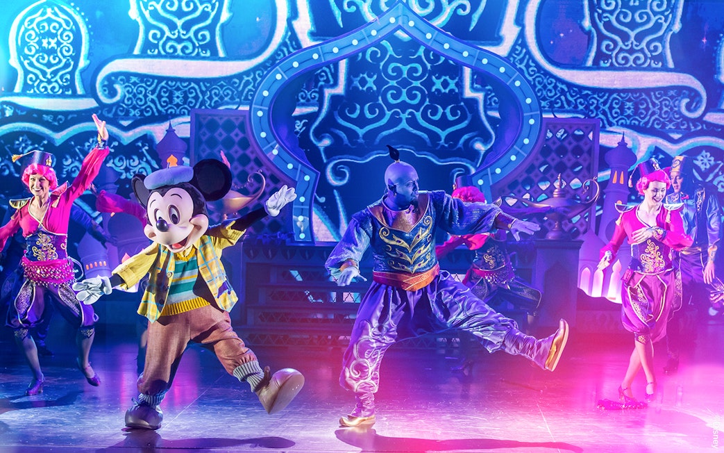 Characters performing a vibrant stage show with colorful costumes and an ornate backdrop.