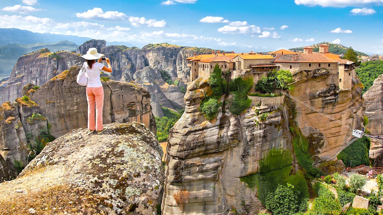 Person photographing Meteora monasteries on rock formations, Greece, during a day tour from Athens.