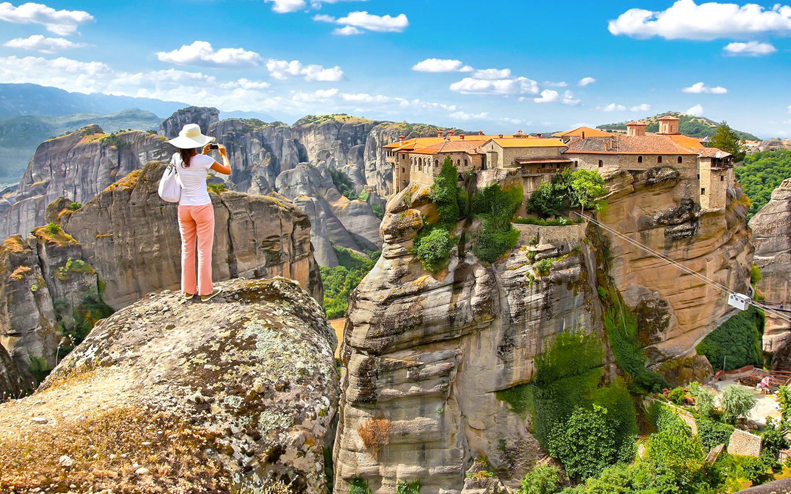 Person photographing Meteora monasteries on rock formations, Greece, during a day tour from Athens.