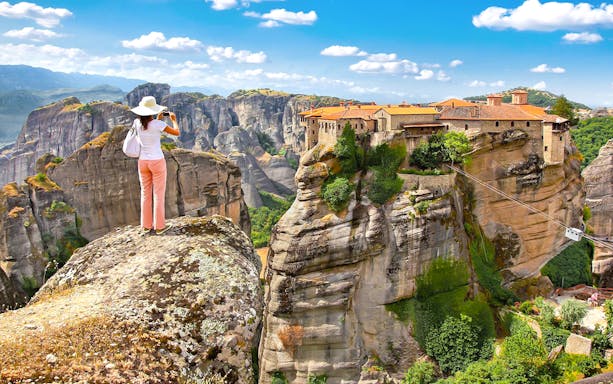 Person photographing Meteora monasteries on rock formations, Greece, during a day tour from Athens.