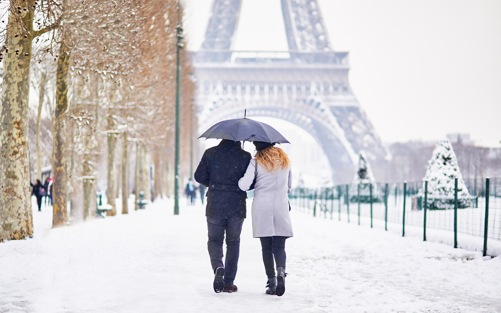 Couple walking under umbrella near Eiffel Tower in snowy Paris winter.