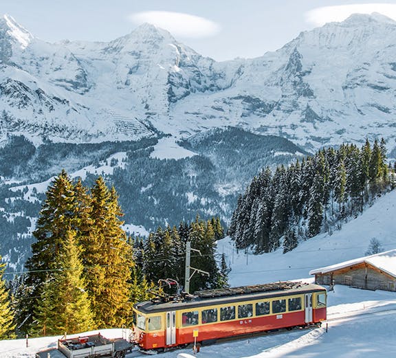 Train traveling through snowy landscape from Interlaken to Jungfraujoch with mountain views.