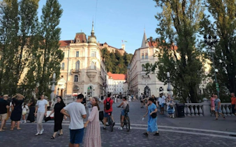 Ljubljana city square with people walking and cycling, historic buildings in the background.