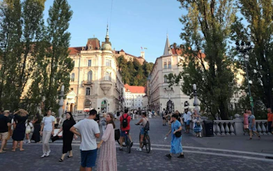 Ljubljana city square with people walking and cycling, historic buildings in the background.