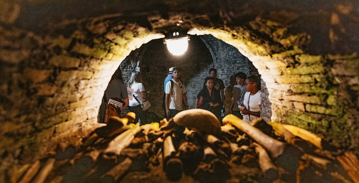 Visitors exploring Roman catacombs with ancient bones in foreground.