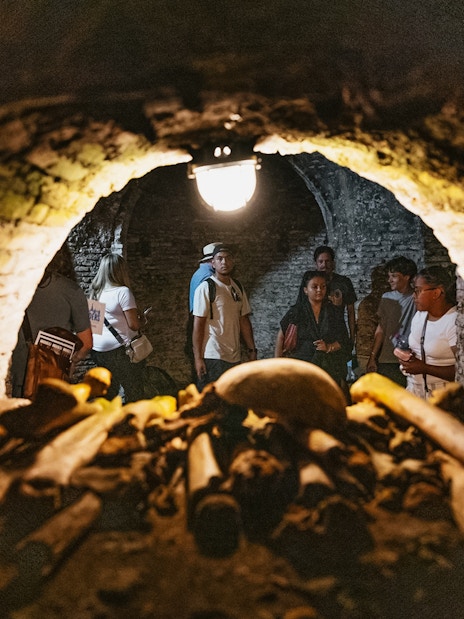 Visitors exploring Roman catacombs with ancient bones in foreground.