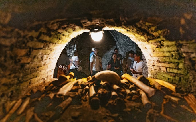 Visitors exploring Roman catacombs with ancient bones in foreground.