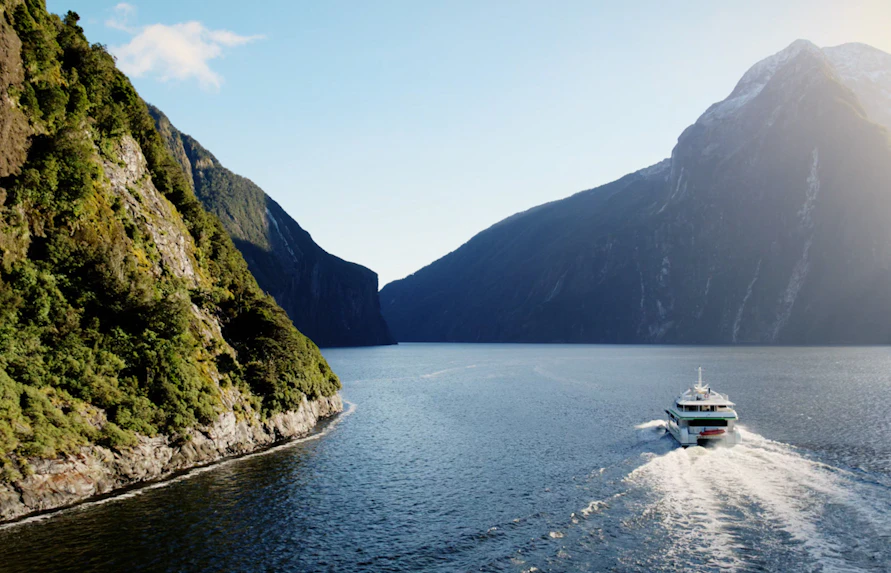 Cruise boat navigating through Milford Sound fjord with towering cliffs in New Zealand.