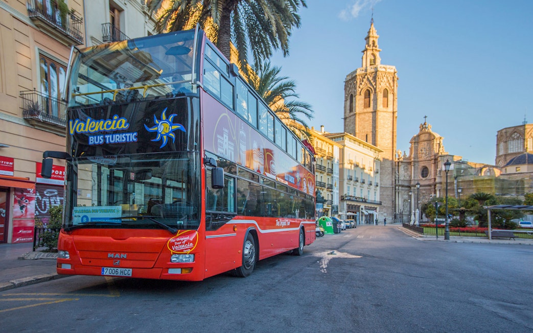 Valencia hop-on hop-off bus near Palma de Mallorca stop with historic buildings in view.
