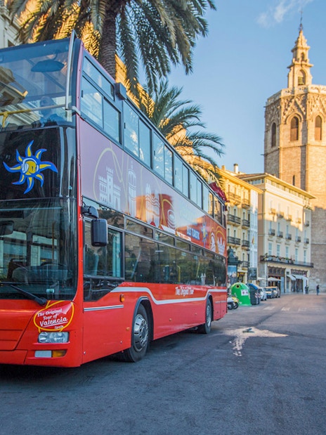 Valencia hop-on hop-off bus near Palma de Mallorca stop with historic buildings in view.