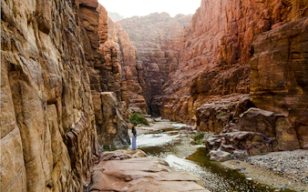 Hiker on Wadi Mujib Siq Trail surrounded by canyon walls, Amman.