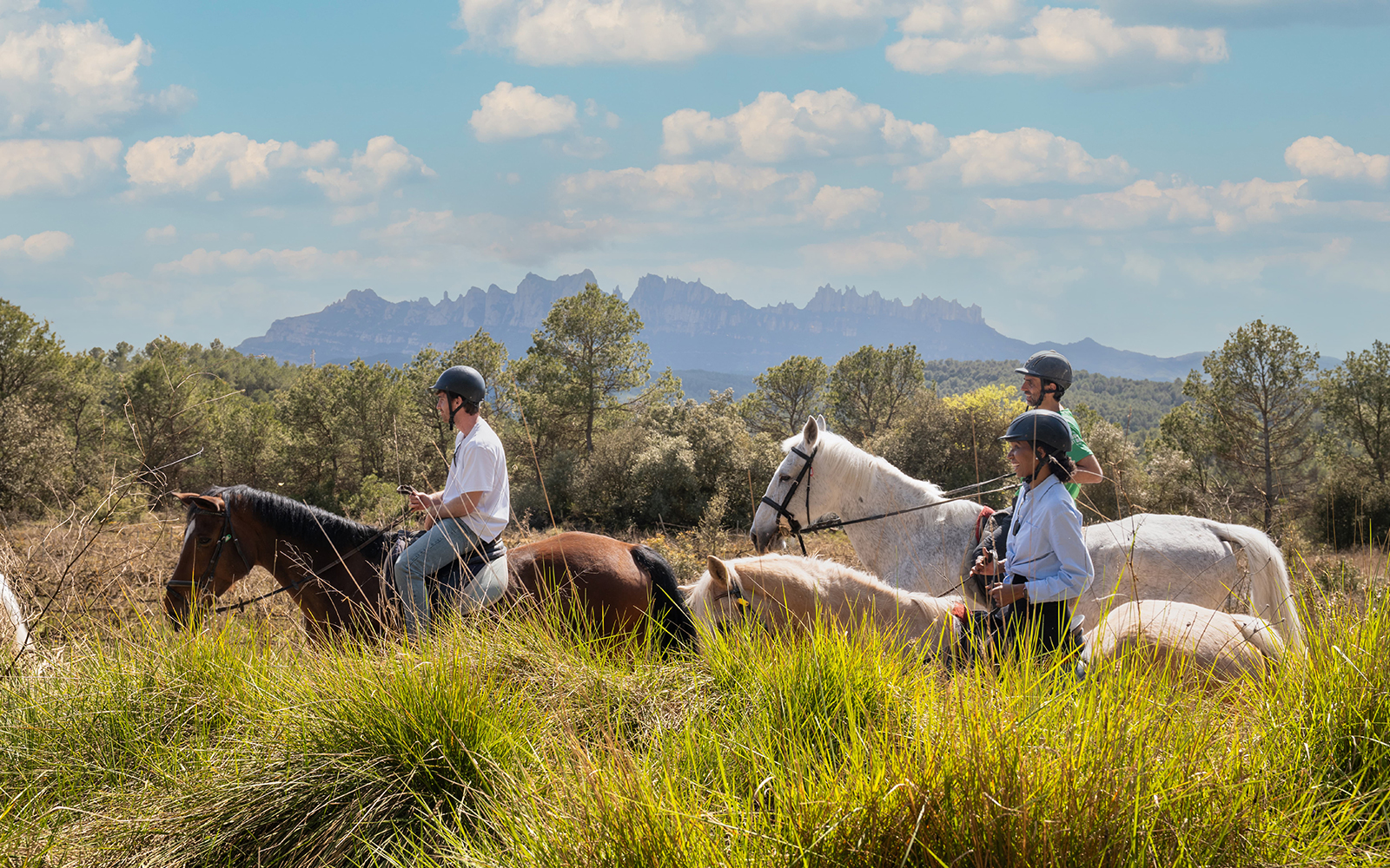 Tourists horseback riding with a guide in Montserrat, Spain, with mountain views.