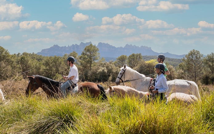 Tourists horseback riding with a guide in Montserrat, Spain, with mountain views.