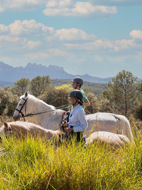 Tourists horseback riding with a guide in Montserrat, Spain, with mountain views.