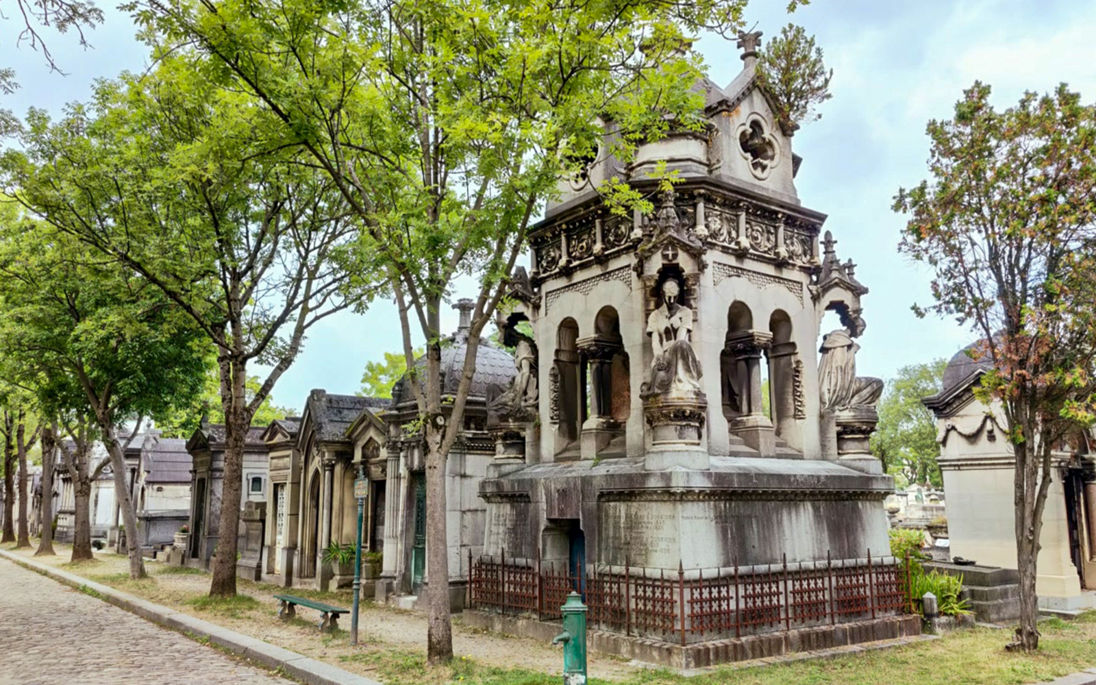 Père-Lachaise Cemetery Paris, ornate tombs and statues along tree-lined path.