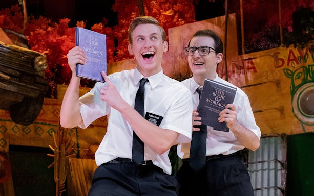 Actors holding "The Book of Mormon" on stage during the musical performance.