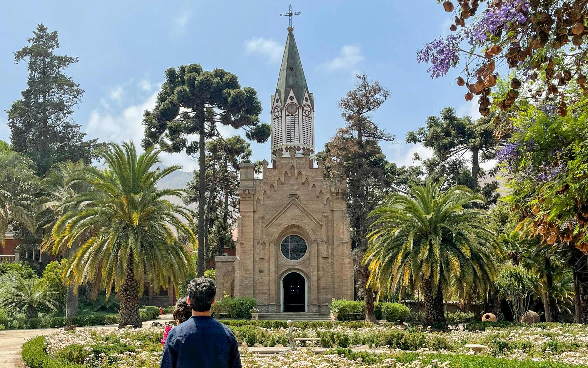 Historic chapel with spire, surrounded by gardens and palm trees at Santa Rita Vineyard.