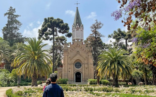 Historic chapel with spire, surrounded by gardens and palm trees at Santa Rita Vineyard.