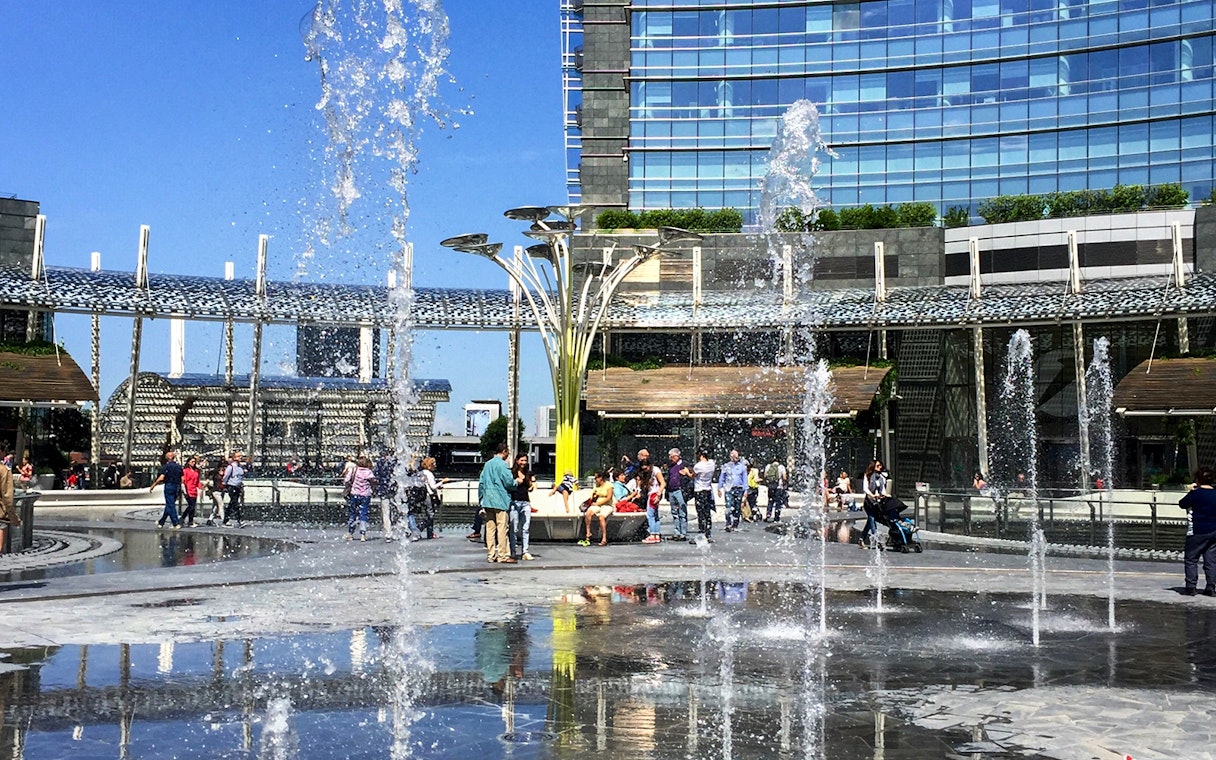 People enjoying fountains at Piazza Gae Aulenti, Milan during hop-on hop-off tour.