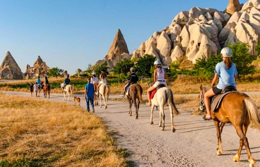 Guests on horseback during sunrise tour in Cappadocia with rock formations in view.