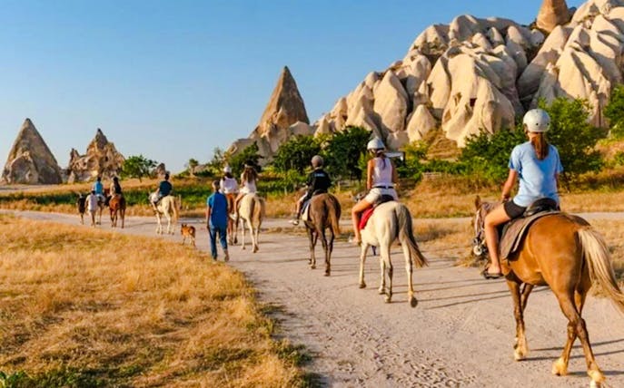 Guests on horseback during sunrise tour in Cappadocia with rock formations in view.