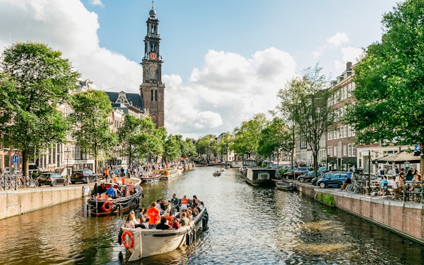 Amsterdam canal with boats and Westerkerk tower during evening guided cruise.