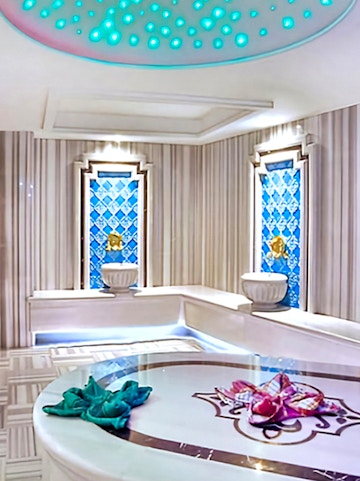 Interior of a private Turkish bath with marble seating and decorative blue tiles.