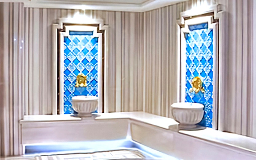 Interior of a private Turkish bath with marble seating and decorative blue tiles.