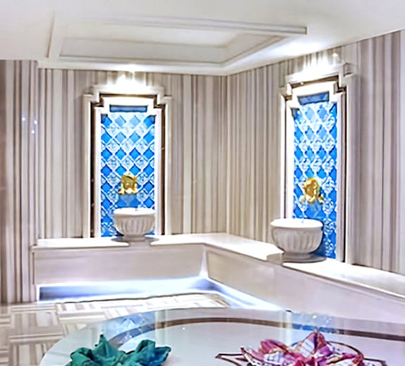 Interior of a private Turkish bath with marble seating and decorative blue tiles.