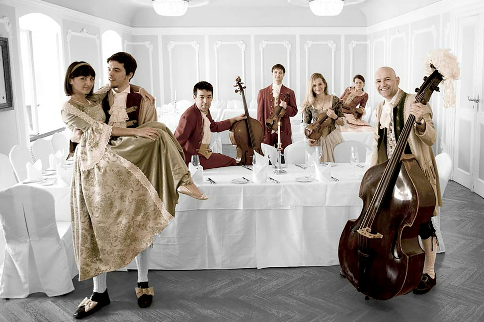 Musicians in period costumes with instruments at a dining table in Salzburg concert setting.