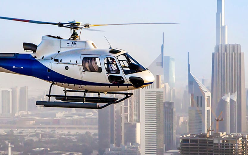 Helicopter flying over Dubai skyline with Burj Khalifa in the background.