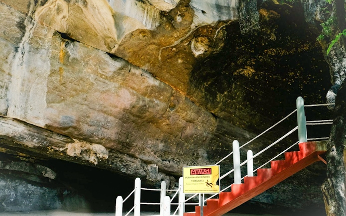 Staircase leading to cave entrance at Kilim Geopark, Langkawi, with caution sign.