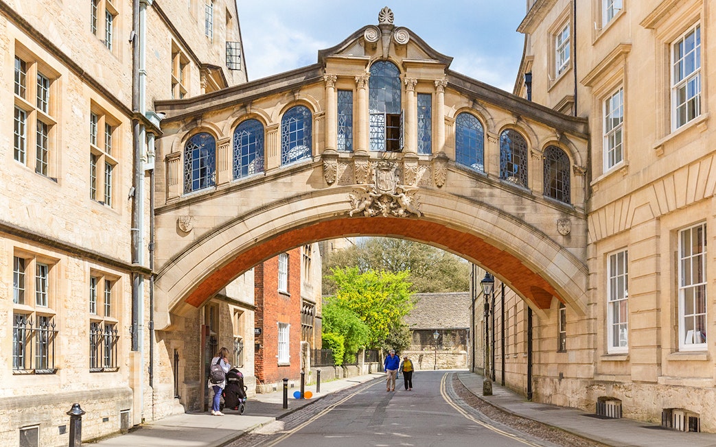 Bridge of Sighs over a street in Oxford, England, with pedestrians walking below.