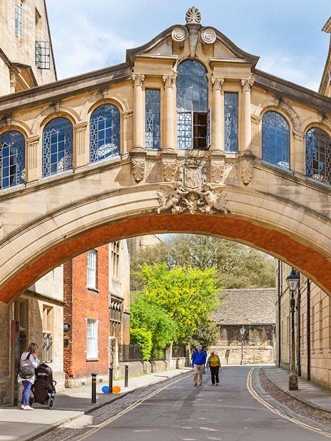 Bridge of Sighs over a street in Oxford, England, with pedestrians walking below.