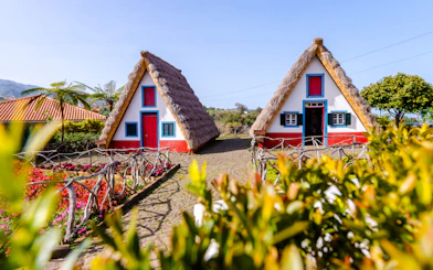 Traditional Santana houses with thatched roofs in Madeira, surrounded by vibrant gardens.