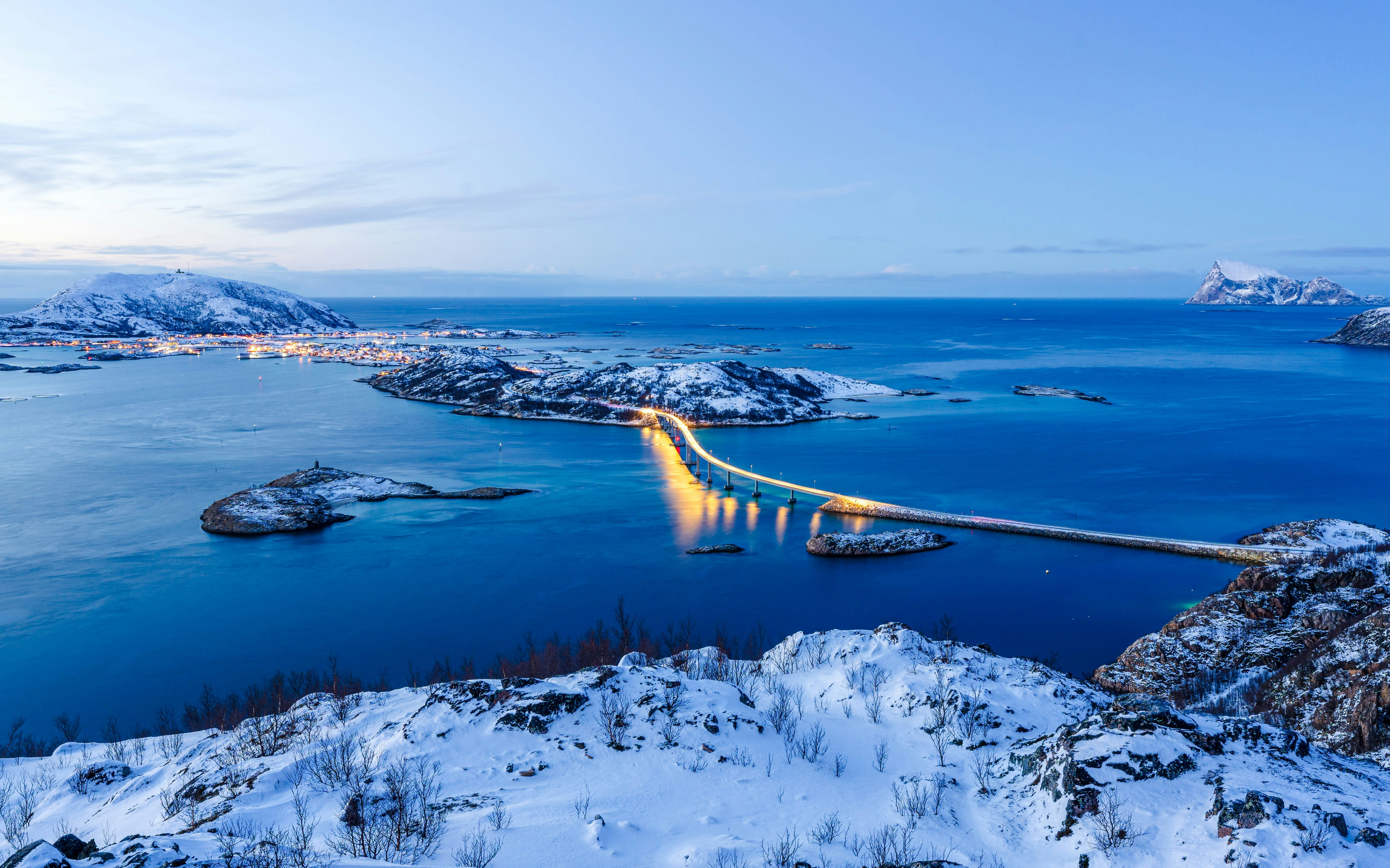 Bridge connecting snow-covered Sommarøy island, Norway, with surrounding islands at dusk.