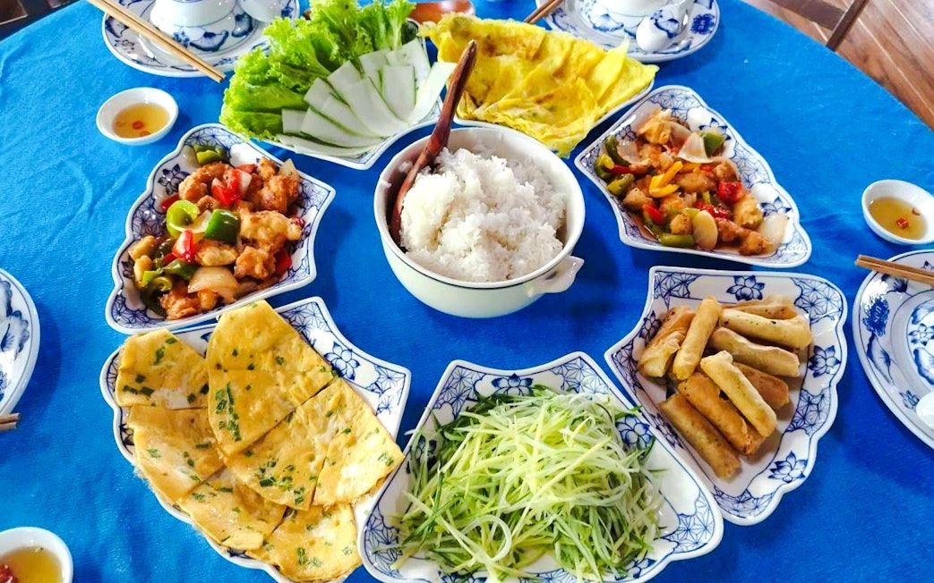 Traditional Vietnamese meal with rice, spring rolls, and vegetables on a round table.