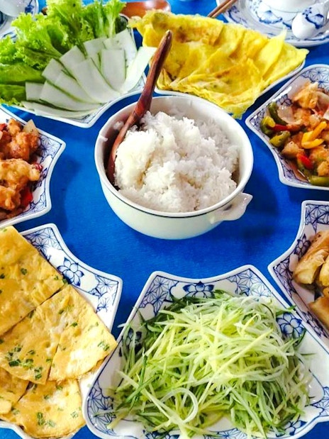 Traditional Vietnamese meal with rice, spring rolls, and vegetables on a round table.