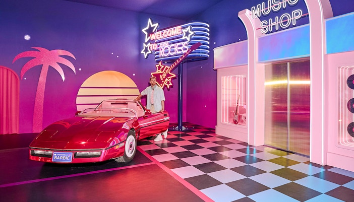 Ken at Barbie The Dream Experience in Amsterdam with a red convertible and neon signs.